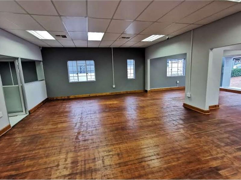 Spacious open-plan retail area featuring polished timber flooring, suspended ceilings with recessed lighting, and large windows with security bars.