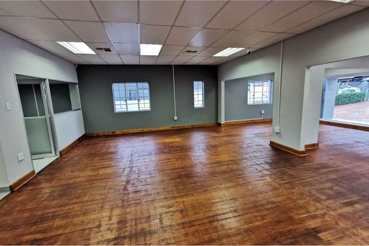 Spacious open-plan retail area featuring polished timber flooring, suspended ceilings with recessed lighting, and large windows with security bars.