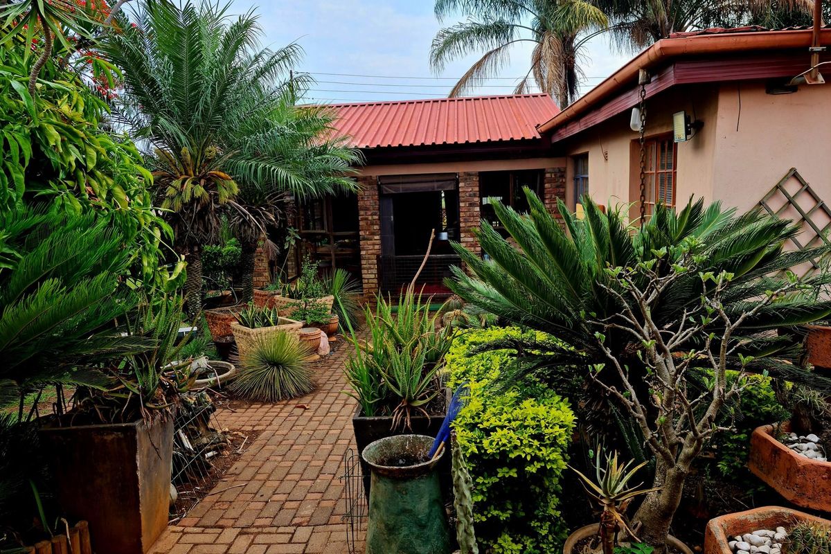A view of the rear garden area featuring a brick pathway, established landscaping, and a building with a red metal roof.