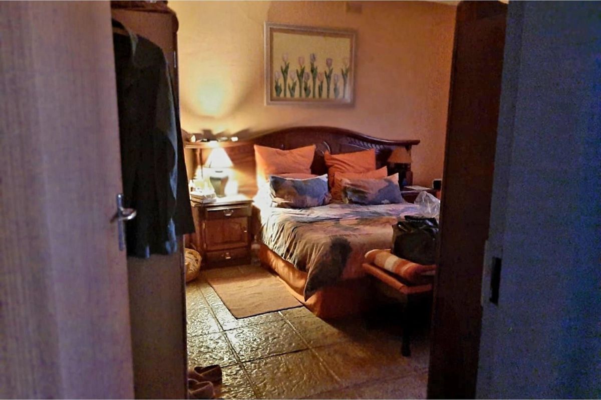 A bedroom featuring tiled flooring and a traditional wooden headboard, viewed from the doorway.
