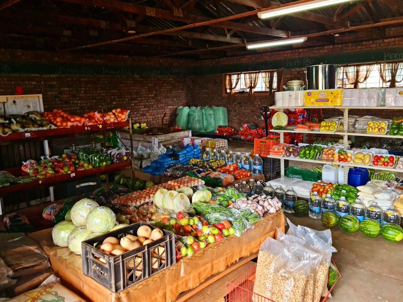 Interior view of a retail produce store featuring exposed brick walls, open timber roof trusses, and fixed shelving units for fresh produce display.