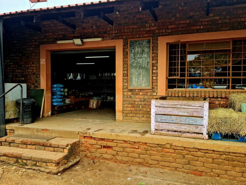 Exterior view of a rustic retail storefront featuring exposed brick walls, a covered entrance, and security bars on the windows.