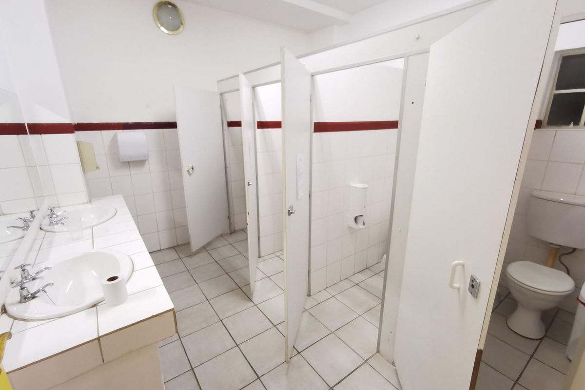 A functional commercial restroom featuring dual vanity basins, multiple partitioned toilet stalls, and tiled flooring throughout.