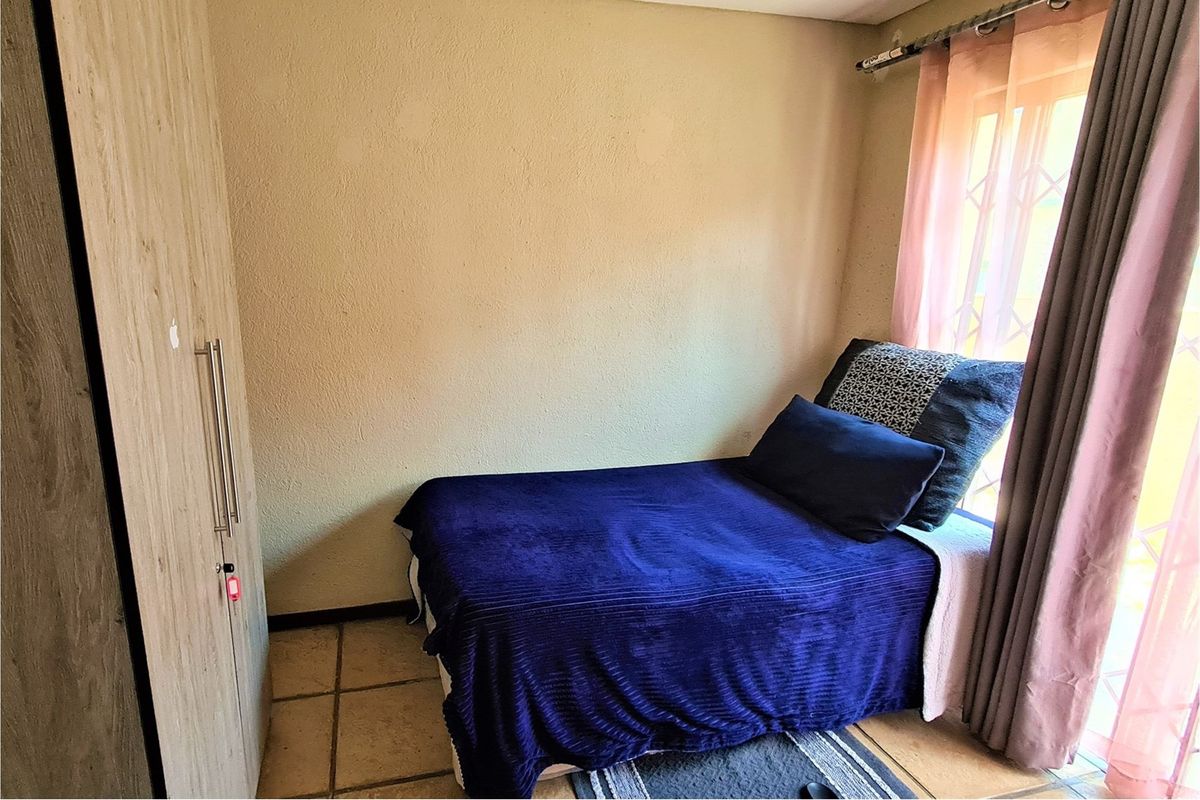 A compact bedroom featuring tiled flooring, a built-in wardrobe, and a window with security bars.