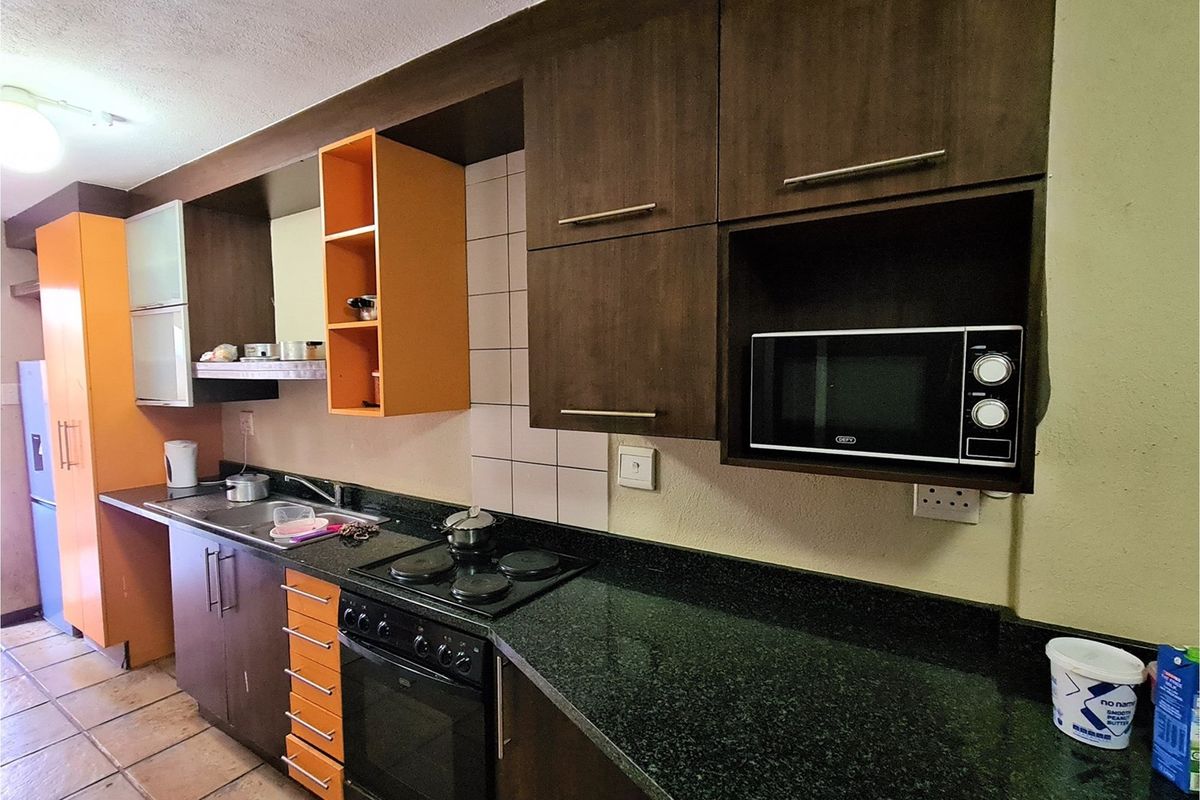 A functional kitchen featuring dark wood and orange cabinetry, granite countertops, a built-in oven, and a hob.