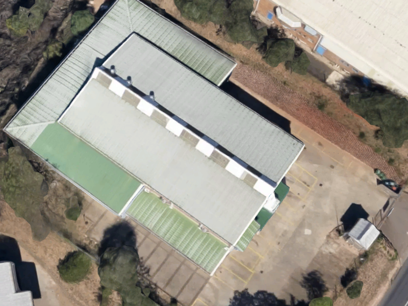 Aerial view of an industrial property featuring a large corrugated metal roof with skylights and an adjacent paved parking area.