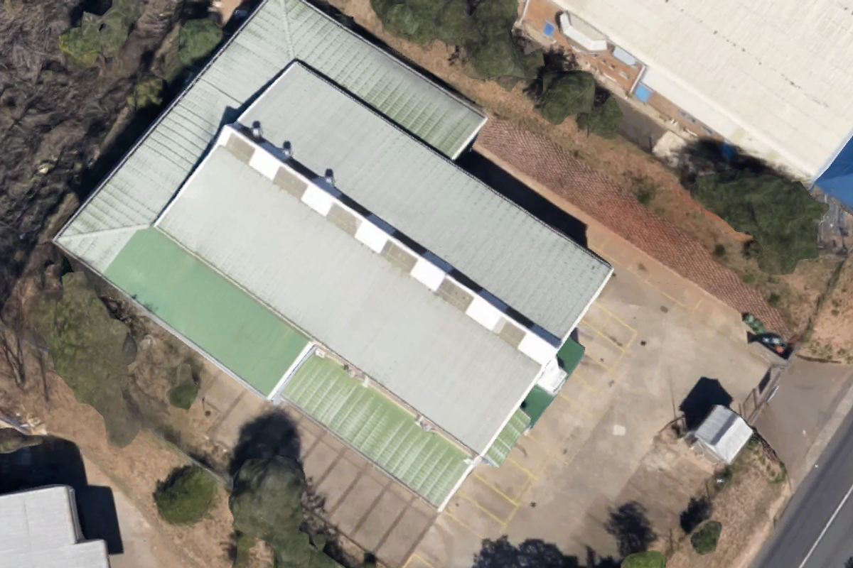 Aerial view of an industrial property featuring a large corrugated metal roof with skylights and an adjacent paved parking area.