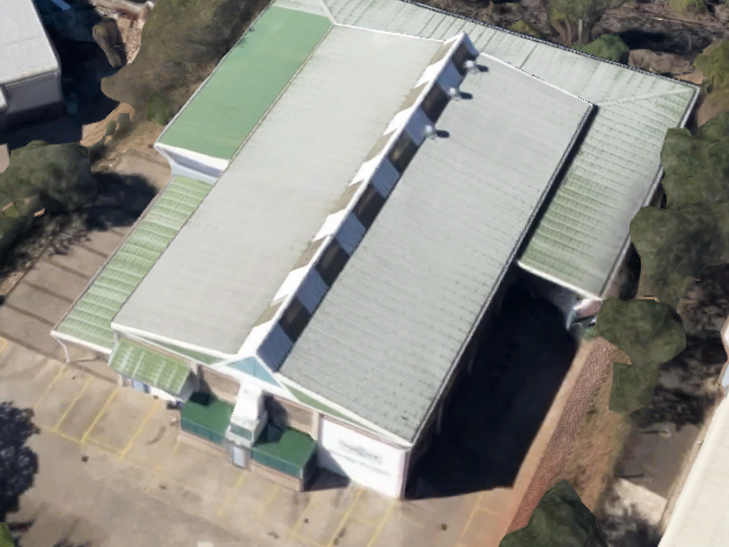 Aerial view of an industrial property featuring a large metal roof with integrated skylights and an adjacent asphalt parking area.
