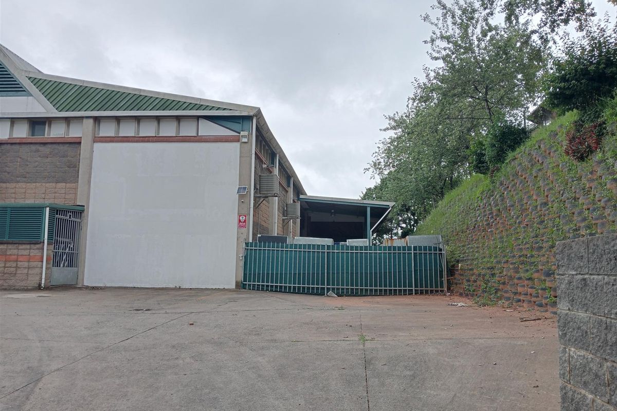 Rear industrial yard featuring a concrete surface, metal security fencing, and a covered loading area adjacent to the warehouse structure.