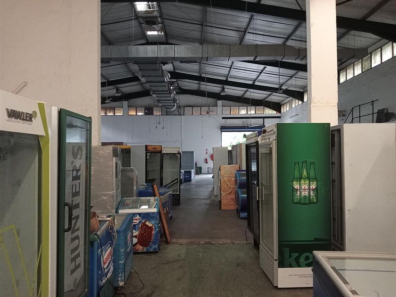Spacious industrial utility area featuring high ceilings with exposed steel trusses, ventilation ducting, and durable concrete flooring, suitable for storage or warehouse operations.