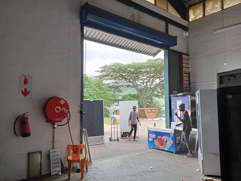 Industrial utility space featuring a large roller shutter door, fire safety equipment, and high-bay lighting, suitable for storage or workshop operations.