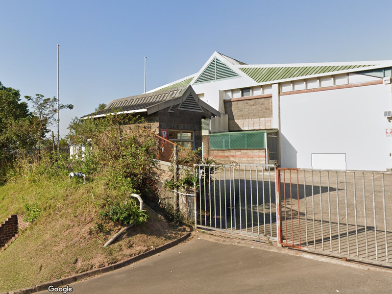 Front exterior view of an industrial property featuring a metal security gate, roller door access, and a brick and metal facade.
