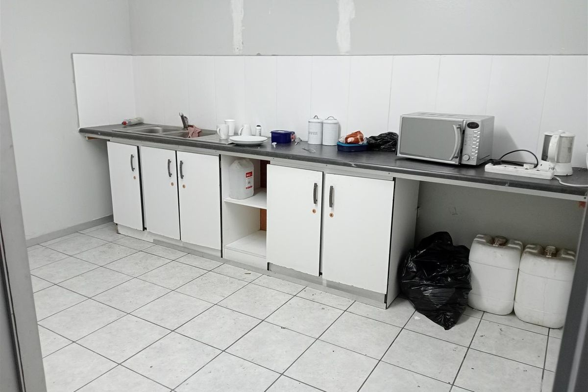 A functional kitchenette area featuring white cabinetry, a stainless steel sink, and tiled flooring, currently requiring minor cosmetic updates to the wall finishes.