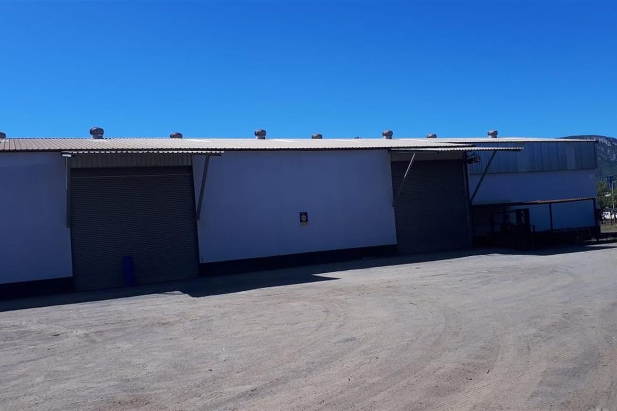 Exterior view of a commercial warehouse facility featuring metal cladding, roller shutter doors, and roof-mounted ventilation turbines.