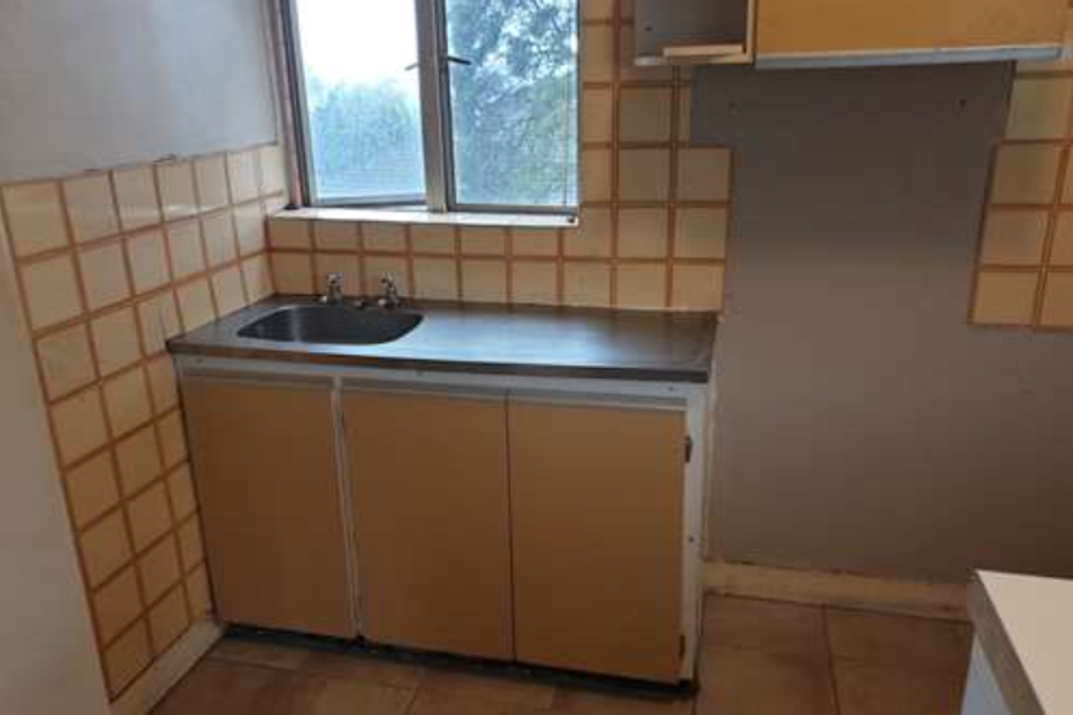 A dated kitchen area featuring a stainless steel sink, basic cabinetry, and tiled splashbacks, requiring renovation and modernization.
