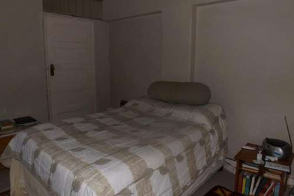 A bedroom featuring a simple layout with a single door and neutral wall finishes, requiring updated lighting and cosmetic improvements.