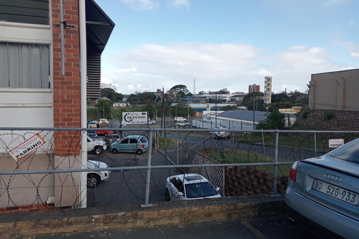 An elevated view of an industrial property exterior featuring a fenced parking area and surrounding commercial infrastructure.