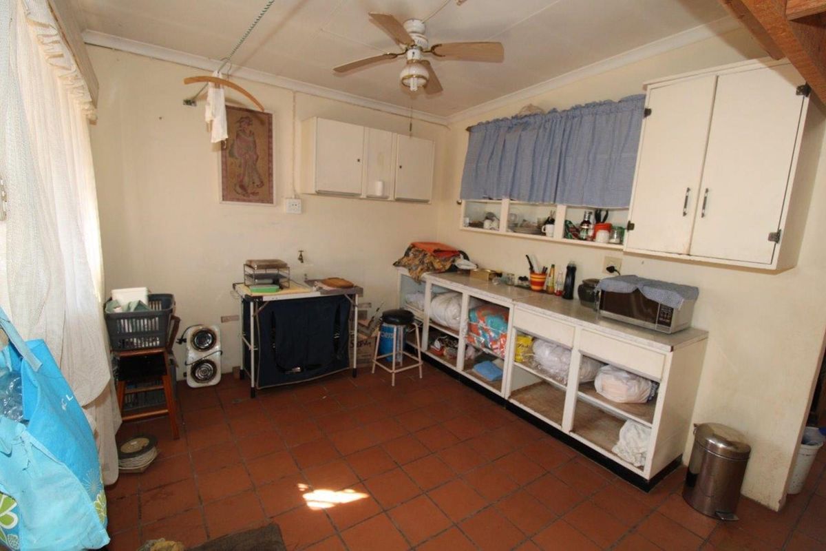 A dated kitchen area featuring terracotta floor tiles, built-in cabinetry, and a ceiling fan, offering potential for a modern renovation.