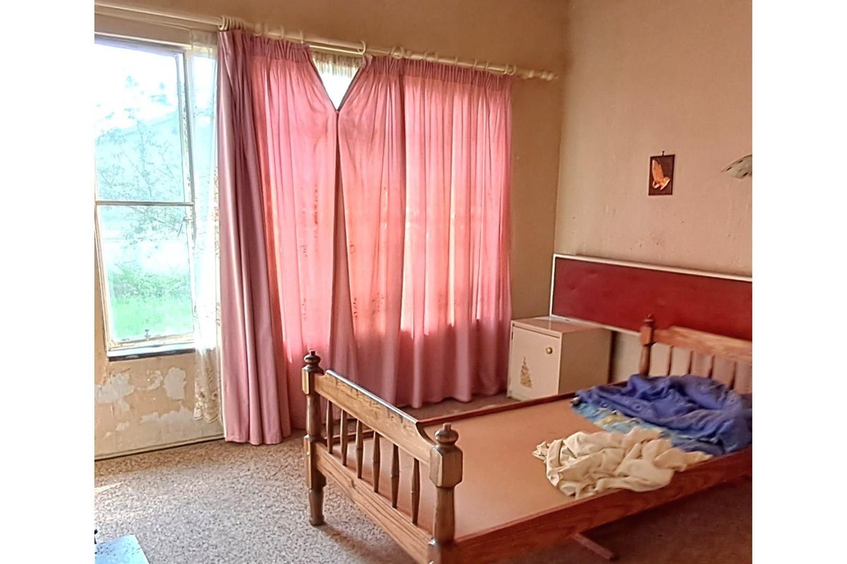 A bedroom featuring a large window with natural light, carpeted flooring, and dated wall finishes requiring cosmetic updates.