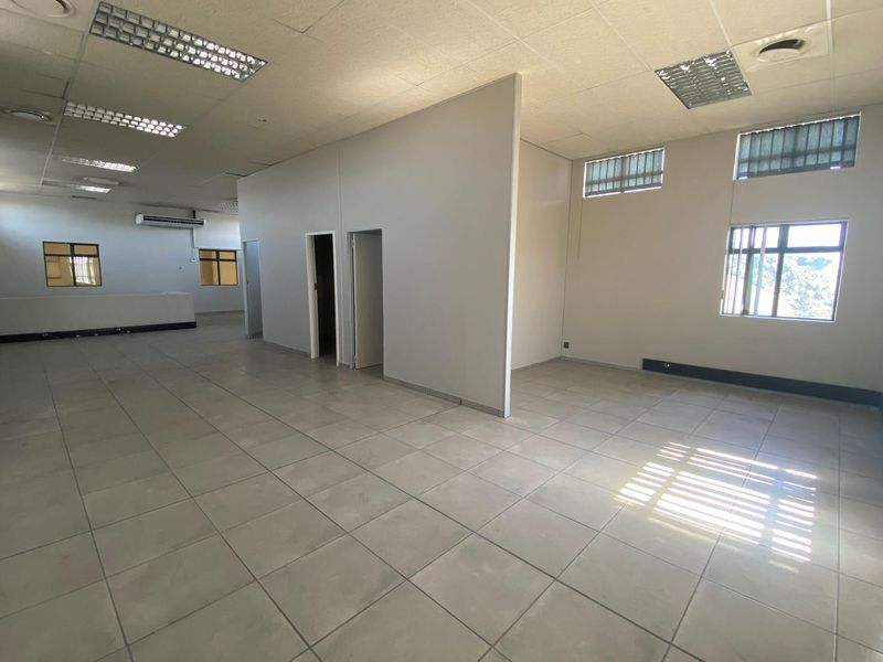 Spacious open-plan office area featuring tiled flooring, recessed fluorescent lighting, partitioned sections, and large windows with security bars.