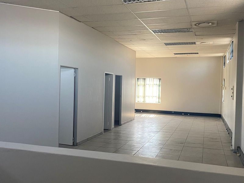 An open-plan office space featuring tiled flooring, a suspended drop ceiling with integrated lighting, and multiple internal doorways.