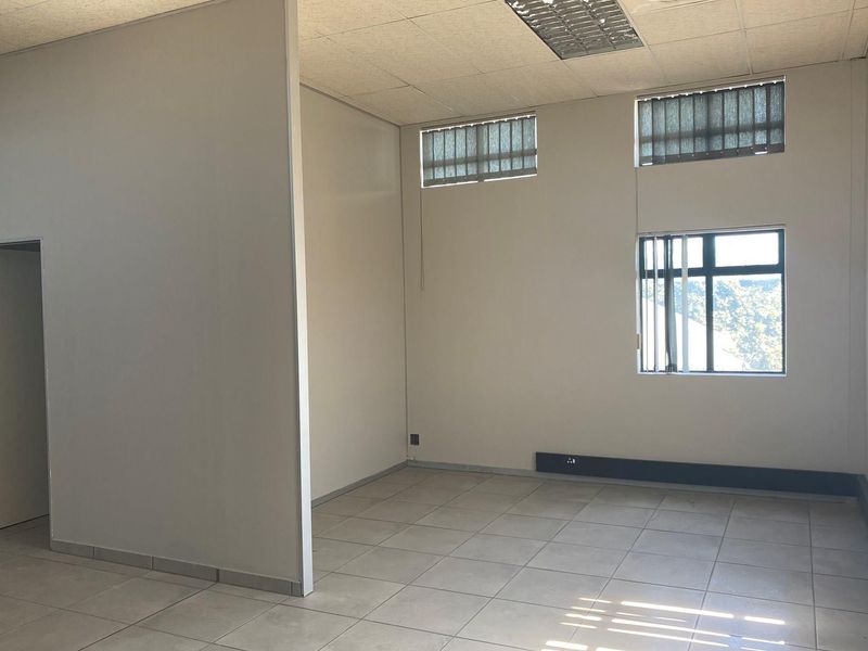 A vacant office space featuring neutral tiled flooring, suspended ceiling tiles, and large windows with vertical blinds, providing a clean and functional work environment.