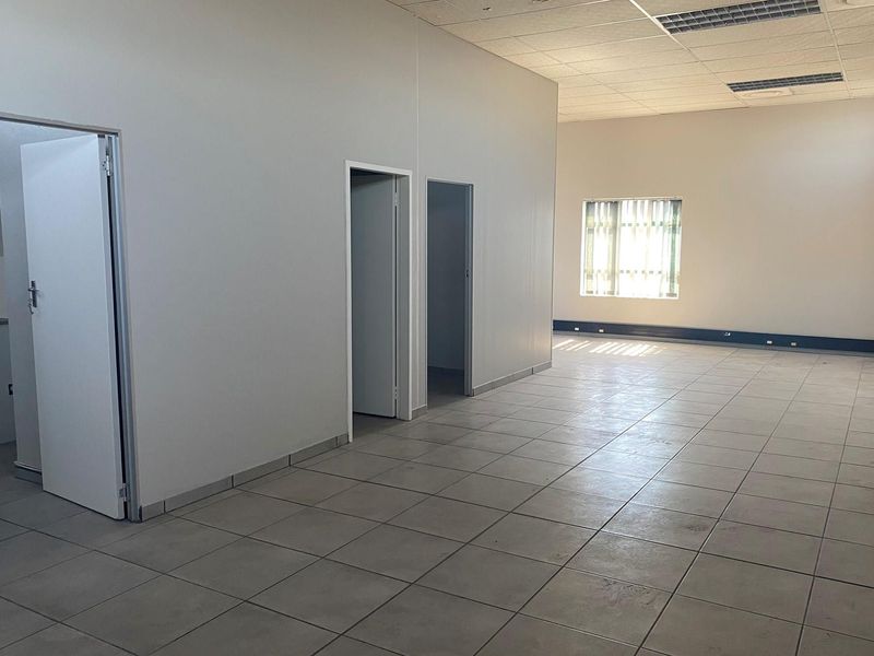 An open-plan office space featuring tiled flooring, recessed ceiling lighting, and multiple internal doorways leading to separate utility or office areas.
