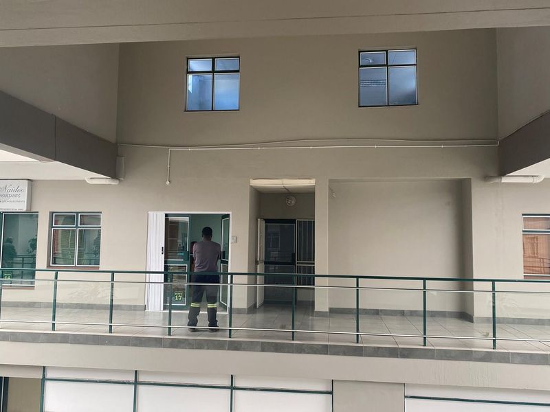 Exterior view of an office building corridor featuring a tiled walkway, metal railings, and multiple office suite entrances.