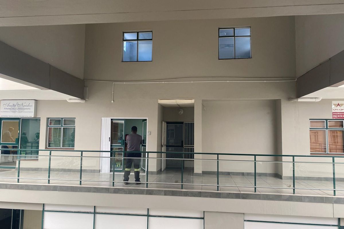 Exterior view of an office building corridor featuring a tiled walkway, metal railings, and multiple office suite entrances.