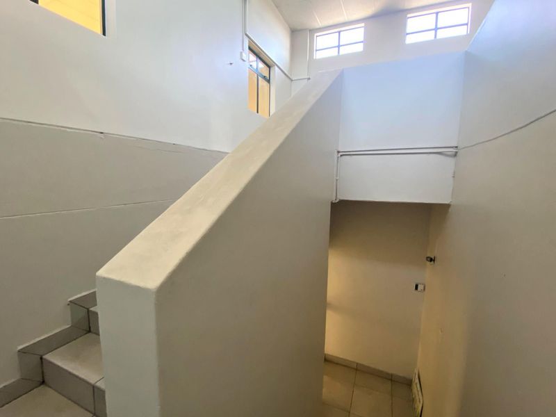 A functional interior staircase area featuring tiled steps, solid balustrades, and high-level windows providing natural light to the office circulation space.