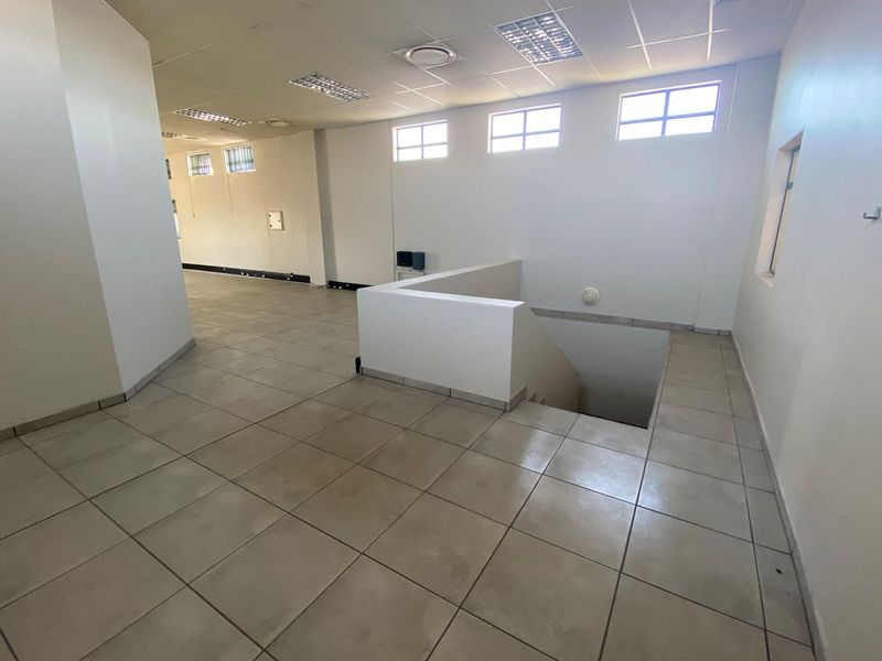 An open-plan office space featuring tiled flooring, recessed ceiling lighting, and a central staircase access point.