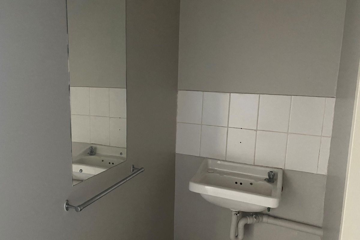 A functional office restroom featuring a wall-mounted basin, tiled splashback, and a wall-mounted mirror with a towel rail.