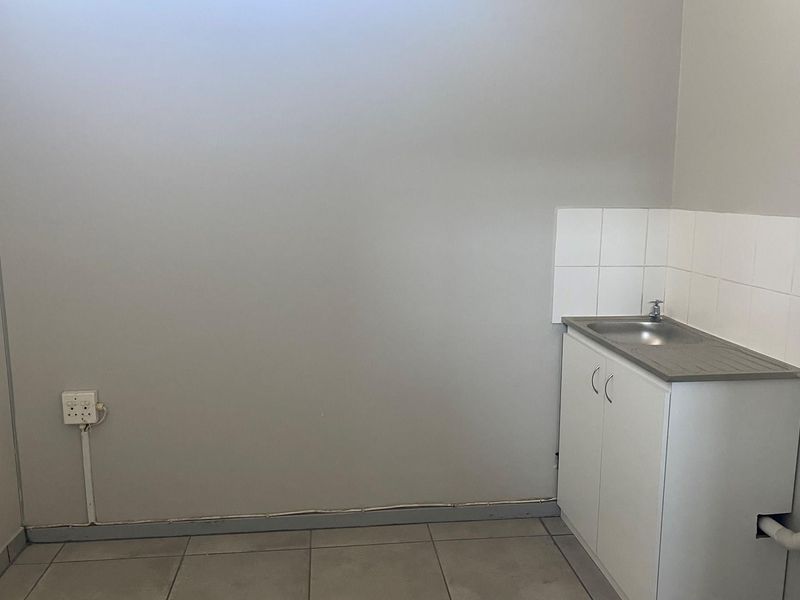 A compact utility space featuring a small kitchenette cabinet with a stainless steel sink, tiled splashback, and tiled flooring.