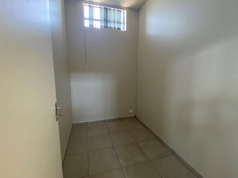 A compact, empty office space featuring neutral wall finishes, tiled flooring, and a high-level window with vertical blinds.
