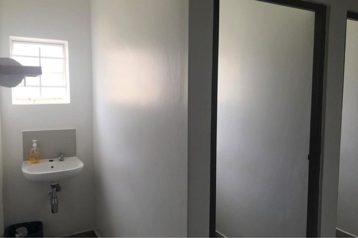 A functional commercial restroom featuring a wall-mounted basin, tiled splashback, and a small window providing natural light.