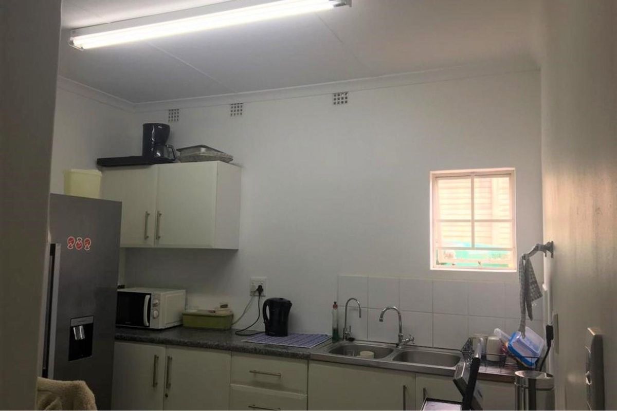 A functional kitchen area featuring built-in cabinetry, a double-basin sink with tiled splashback, and overhead fluorescent lighting.