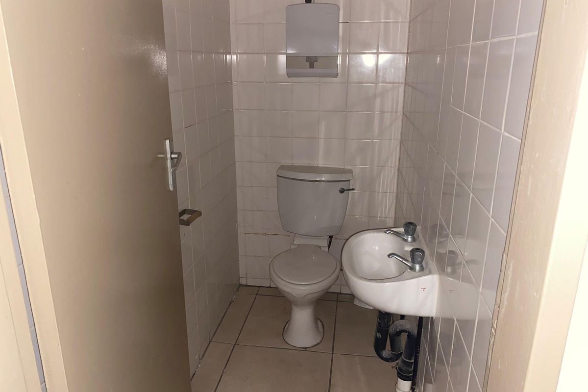 A compact office restroom featuring tiled walls, a standard toilet, and a wall-mounted basin with exposed plumbing.