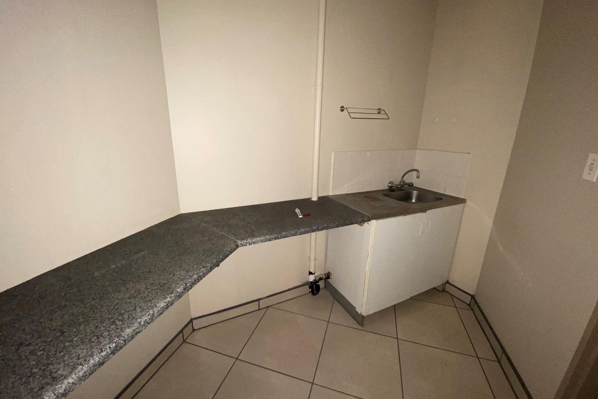 A functional kitchenette area featuring a single basin sink, built-in cabinetry, and a stone-look countertop, suitable for office tea station or utility use.