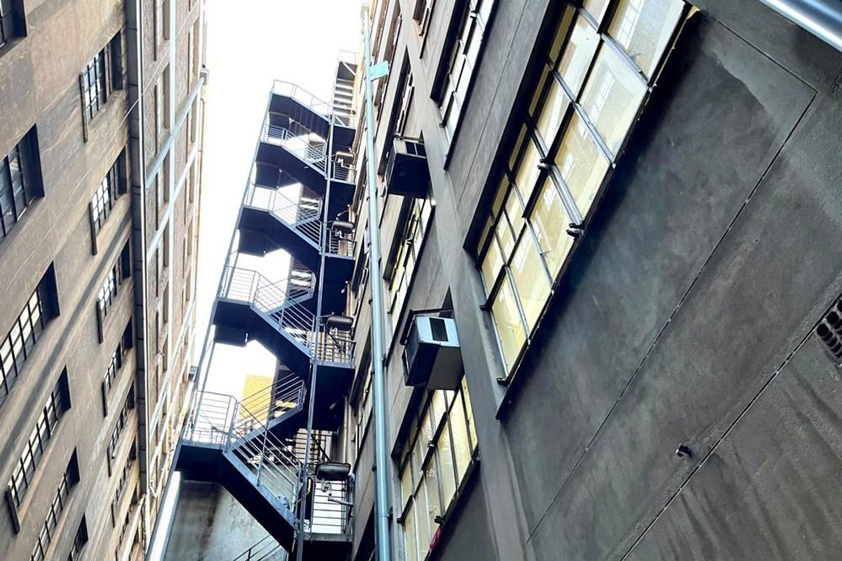 Exterior view of a commercial building featuring a multi-level metal fire escape staircase and industrial-style windows along the side facade.