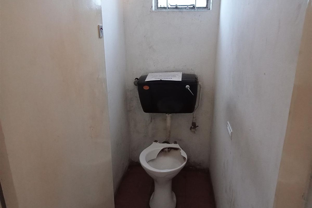 A small, dated restroom facility featuring a damaged toilet bowl and high-level cistern, requiring significant maintenance and refurbishment.