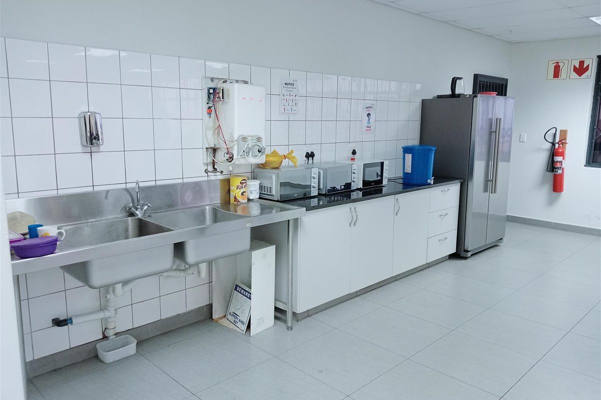 Industrial kitchen area featuring a double stainless steel sink, white cabinetry, tiled splashback, and tiled flooring in a functional workspace.