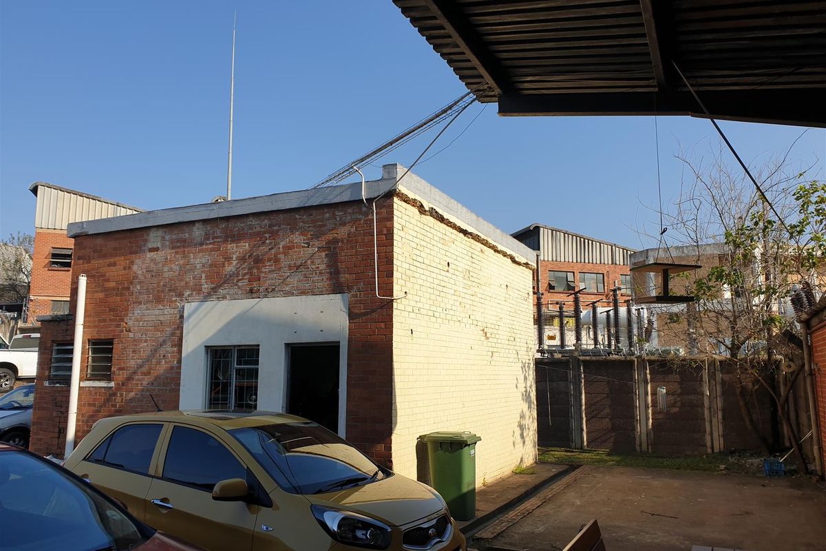 Exterior view of an industrial brick building featuring a covered outdoor area and adjacent parking space.