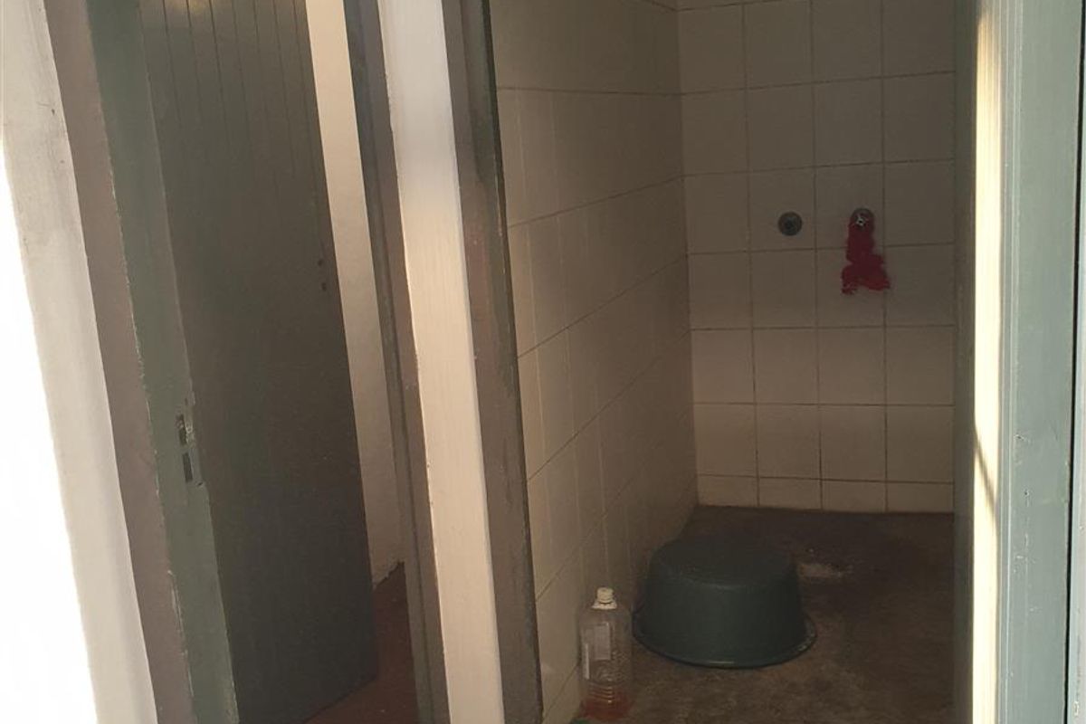 A basic industrial shower cubicle featuring tiled walls and a concrete floor, requiring maintenance and cosmetic updates.
