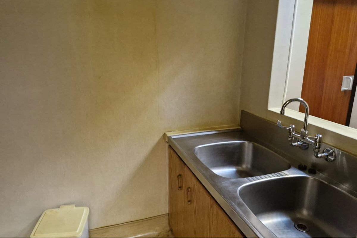 A functional kitchenette area featuring a stainless steel double sink, wall-mounted faucet, and built-in wooden cabinetry.