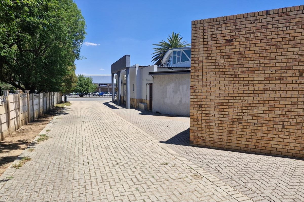 A paved rear exterior area featuring a face brick boundary wall and concrete structural pillars, providing access to the office building.