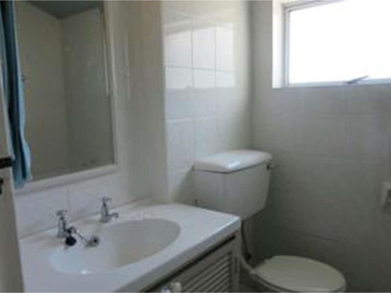 A functional bathroom featuring a vanity cabinet with a ceramic basin, wall-mounted mirror, toilet, and tiled wall finishes.
