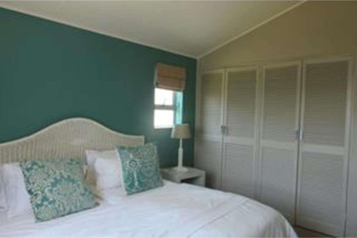 A bedroom featuring built-in cupboards with louvered doors and a sloped ceiling, accented by a teal feature wall.