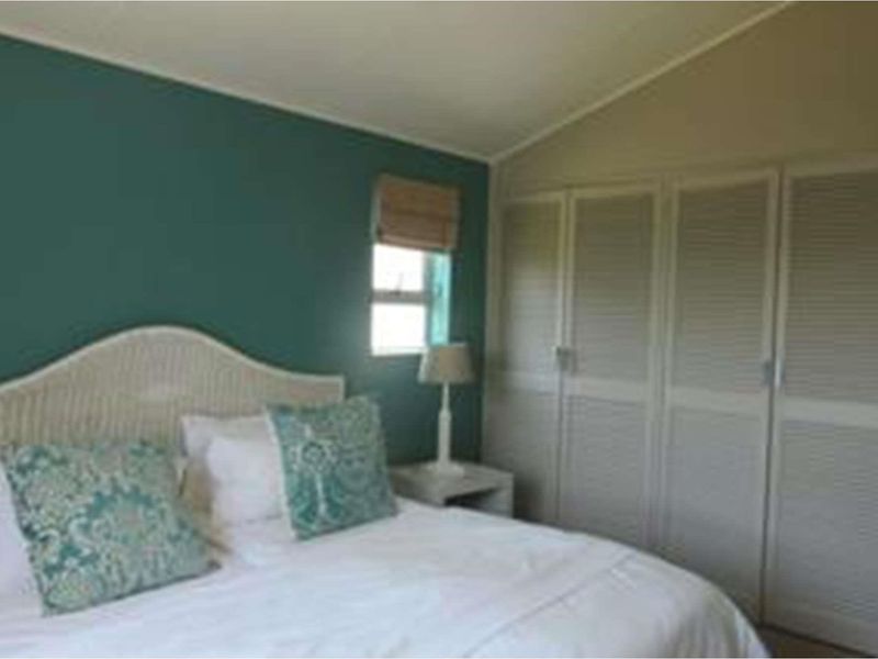 A bedroom featuring built-in cupboards with louvered doors and a sloped ceiling, accented by a teal feature wall.