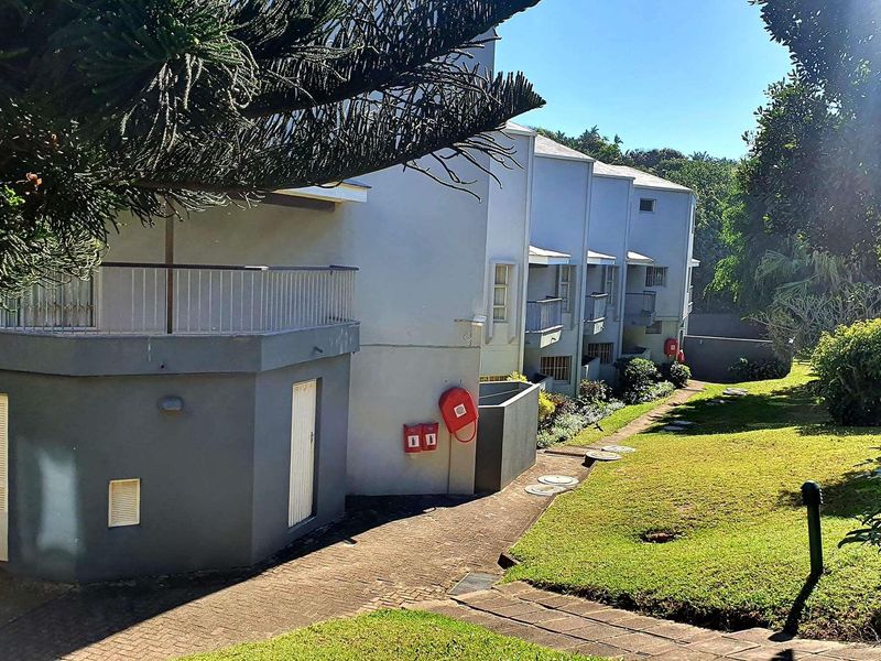 Rear view of the commercial property complex featuring paved walkways, landscaped garden areas, and multiple balconies with fire safety equipment installed.