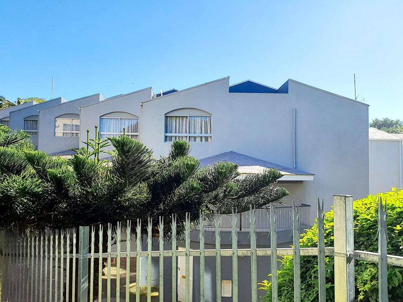 Rear view of a multi-unit commercial building featuring a pitched roof design, balcony with metal railing, and secure perimeter fencing.
